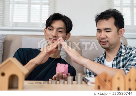 LGBTQ couple playfully creating a home symbol with their hands while planning savings for a future home. 130550744