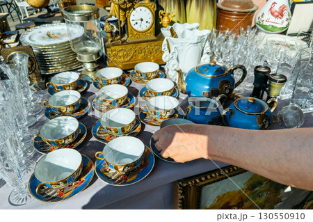 Vintage porcelain tea set with matching cups, saucers, and teapots displayed at a flea market. Luxury for less, antique gold accents, flea market treasures, sustainable luxury 130550910