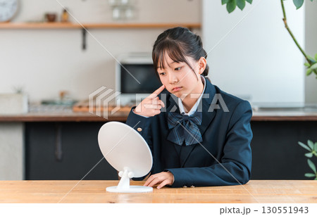 家のリビングで鏡を見ながら落ち込む制服姿の小学生,中学生の女の子(ニキビ,肌荒れ,肌トラブル) 家のリビングで鏡を見ながら落ち込む制服姿の小学生,中学生の女の子(ニキビ,肌荒れ,肌トラブル) 130551943