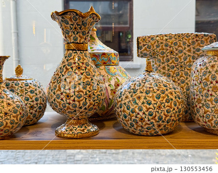 Ornamental ceramic vases with floral golden patterns arranged on wooden shelves. Cultural heritage, handmade craftsmanship, and decorative artistry reflecting elegance and tradition. 130553456