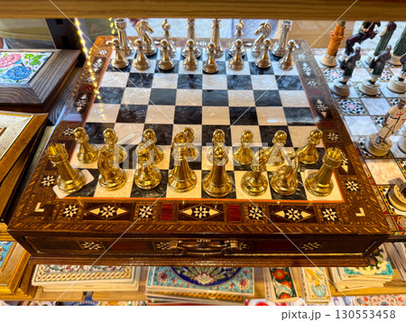 Elegant chessboard with golden and silver pieces on a wooden inlaid base. Strategy, intelligence, and craftsmanship blending art and competitive tradition in one design. 130553458
