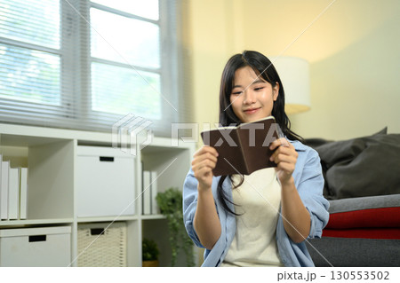 Young woman reviewing her travel journal at home while preparing for an upcoming trip 130553502