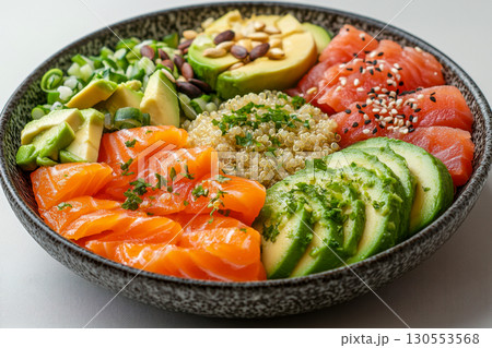 Colorful healthy poke bowl with fresh salmon, avocado, quinoa, and green onions. Nutritious meal featuring sesame seeds, pine nuts, and pumpkin seeds. Colorful healthy poke bowl with fresh salmon, avocado, quinoa, and green onions. Nutritious meal featuring sesame seeds, pine nuts, and pumpkin seeds. 130553568