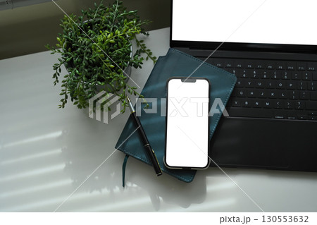 Smartphone with blank screen on notebook, and laptop, with plant decor on desk Smartphone with blank screen on notebook, and laptop, with plant decor on desk 130553632