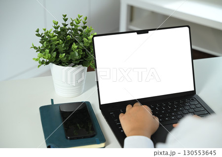 Close up of person working on laptop with blank white screen for mockup design 130553645