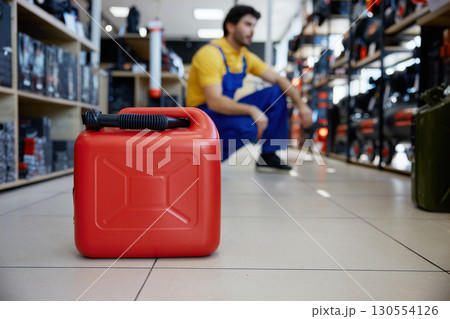 A bright red gas can in a work store with a man worker on a background 130554126