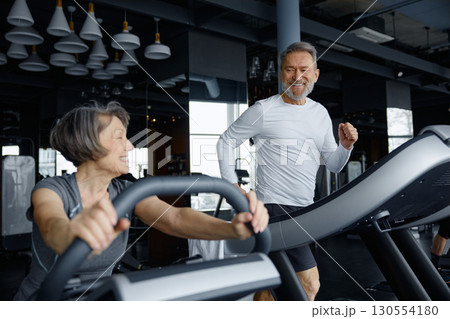 Elderly couple are exercising in gym setting using a training machines together Elderly couple are exercising in gym setting using a training machines together 130554180