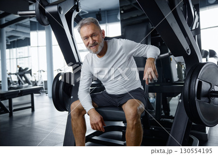 An older gentleman is resting on a training machine in contemporary gym 130554195