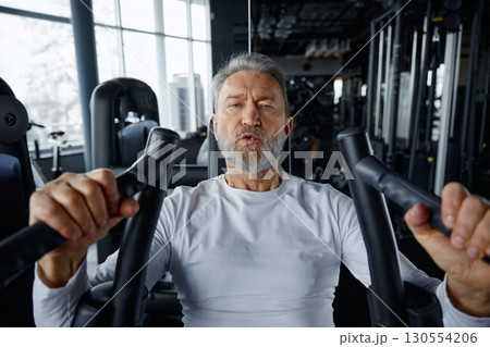 Portrait of an older man hardly training in a training machine in a gym 130554206