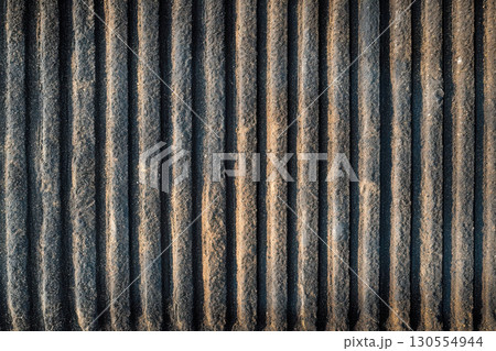 Textured dark industrial metal surface background with vertical grooves. Rough worn gritty dirty material showing strong shadows and bright light. Abstract pattern. 130554944