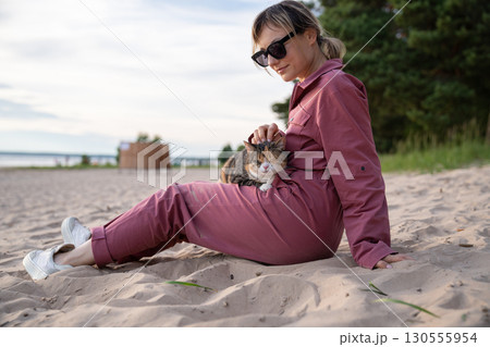 Woman on beach petting stressed cat on lap during walk. Animal stress relief on stroll, calming pet 130555954