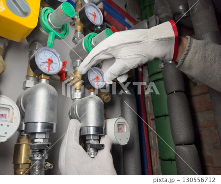 Plumbing pressure gauge with valve and pipe for system adjustment. Technician hand in gloves Plumbing pressure gauge with valve and pipe for system adjustment. Technician hand in gloves 130556712