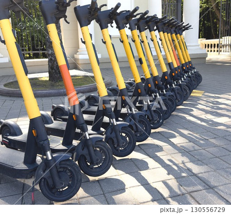Row of yellow electric scooters parked neatly on a paved area in the city, ready for urban commuting Row of yellow electric scooters parked neatly on a paved area in the city, ready for urban commuting 130556729