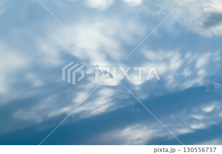 Soft, wispy stratocumulus clouds spread across a pale blue sky, with gentle shading creating a 130556737