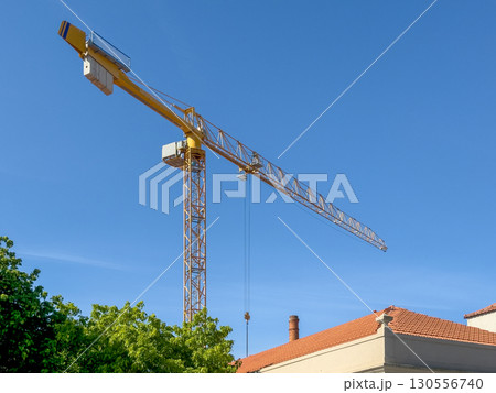 Tall construction crane above a red roofed building and green trees under a clear blue sky. urban 130556740