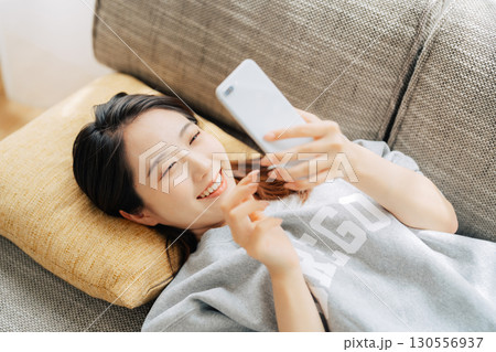 ソファに寝転がってスマホを使う女性　 130556937