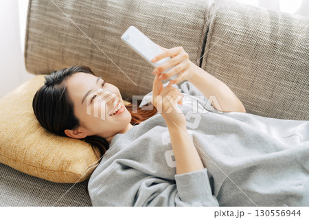 ソファに寝転がってスマホを使う女性 ソファに寝転がってスマホを使う女性 130556944