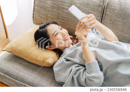 ソファに寝転がってスマホを使う女性　 130556946