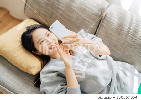 ソファに寝転がってスマホを使う女性  ソファに寝転がってスマホを使う女性  130557054