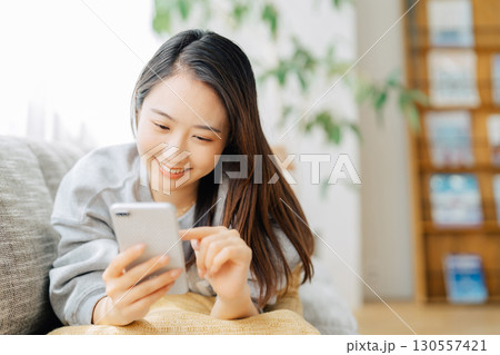 ソファに寝転がってスマホを使う女性　 130557421