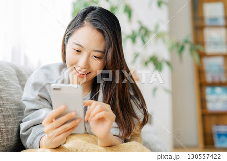 ソファに寝転がってスマホを使う女性　 130557422