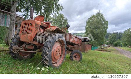 Old red rusty russian tractor t 16 parked beside gravel road in rural area surrounded by trees and old buildings during a cloudy afternoon Old red rusty russian tractor t 16 parked beside gravel road in rural area surrounded by trees and old buildings during a cloudy afternoon 130557897