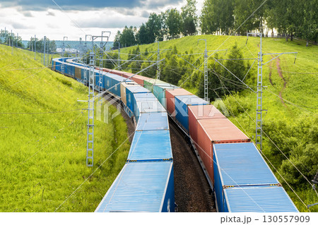 Railway container transportation . Two freight trains with containers are traveling in parallel among green hills in nature in a beautiful place. Railway container transportation . Two freight trains with containers are traveling in parallel among green hills in nature in a beautiful place. 130557909