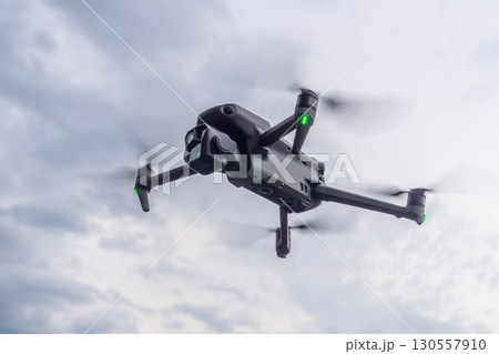 Drone soaring over a scenic landscape showcasing modern technology and nature's beauty during an overcast afternoon. A black quadcopter in close-up against a flying cloudy sky 130557910