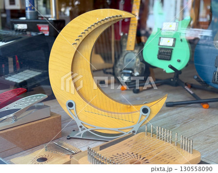 Wooden crescent-shaped string instrument displayed in a shop window with guitars. Creative design, musical craftsmanship, and artistic heritage blending tradition and innovation. Wooden crescent-shaped string instrument displayed in a shop window with guitars. Creative design, musical craftsmanship, and artistic heritage blending tradition and innovation. 130558090
