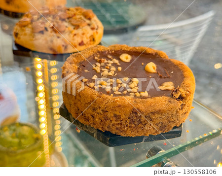 Chocolate tart with hazelnut topping displayed on a glass shelf in a bakery. Gourmet dessert, sweet indulgence, and artisan pastry tradition of handmade treats. Chocolate tart with hazelnut topping displayed on a glass shelf in a bakery. Gourmet dessert, sweet indulgence, and artisan pastry tradition of handmade treats. 130558106