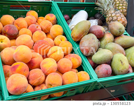 Fresh peaches and mangoes arranged in green crates at a market stall. Seasonal produce, agricultural harvest, and tropical fruit trade reflecting natural abundance. Fresh peaches and mangoes arranged in green crates at a market stall. Seasonal produce, agricultural harvest, and tropical fruit trade reflecting natural abundance. 130558123