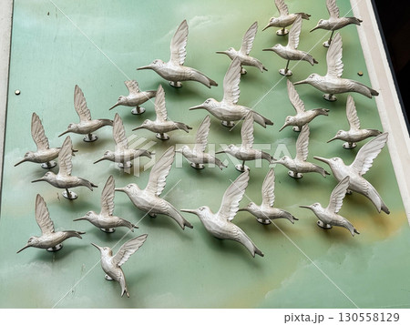 White bird sculptures attached to a green wall creating an impression of flock in flight. Symbolism of freedom, motion, and collective unity represented in design. 130558129