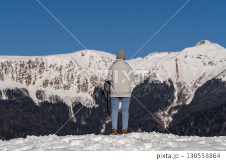 Snow Mountains Person Winter: Solo hiker admires snow-capped mountain range, sunny day, scenic vista. 130558864