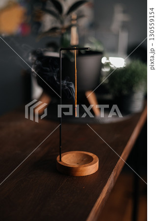 incense stick smokes on a wooden stand on a dark background. Aromatherapy, Smoke while burning incense. smoke for prayers and meditation. prayer to buddha. incense for relaxation and yoga incense stick smokes on a wooden stand on a dark background. Aromatherapy, Smoke while burning incense. smoke for prayers and meditation. prayer to buddha. incense for relaxation and yoga 130559154