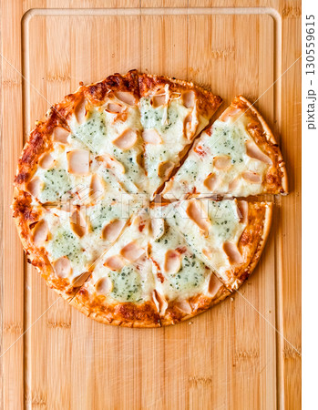 Sliced pizza with visible pieces and toppings on wooden board. Sharing, leisure and culinary enjoyment in everyday dining. Sliced pizza with visible pieces and toppings on wooden board. Sharing, leisure and culinary enjoyment in everyday dining. 130559615