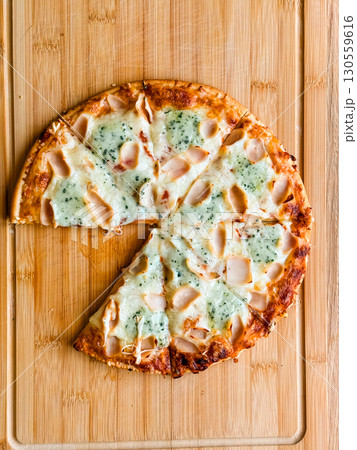 Sliced pizza with visible pieces and toppings on wooden board. Sharing, leisure and culinary enjoyment in everyday dining. Sliced pizza with visible pieces and toppings on wooden board. Sharing, leisure and culinary enjoyment in everyday dining. 130559616