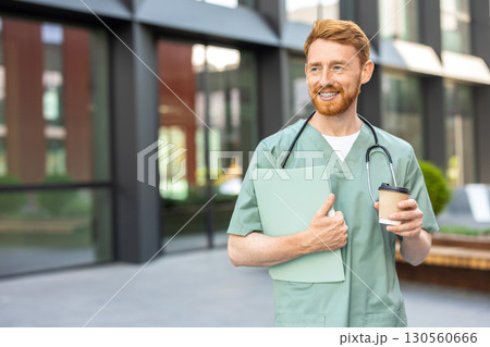 Man physician in scrubs standing near hospital with cup and folder 130560666