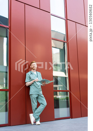 Man doctor studying papers in open medical chart near hospital building 130560682