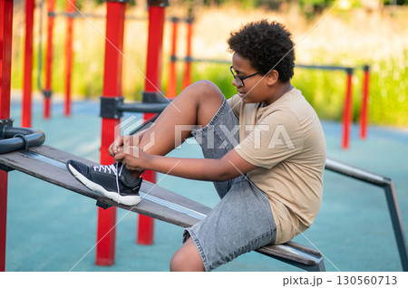 Teen at the playground sitting and tying his sneaker Teen at the playground sitting and tying his sneaker 130560713
