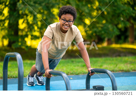 Curly-haired teen exercising at the playground and looking excited 130560721