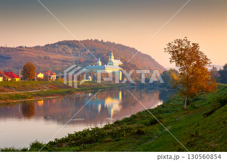 mukachevo, ukraine - 06 nov, 2015: urban landscape with river and trees in autumn. reflection of a monastery in the distance. beautiful travel destination of transcarpathia mukachevo, ukraine - 06 nov, 2015: urban landscape with river and trees in autumn. reflection of a monastery in the distance. beautiful travel destination of transcarpathia 130560854