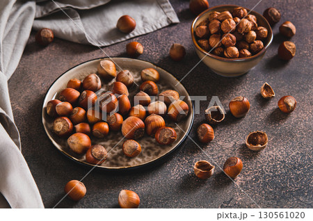 Nutritious unpeeled hazelnuts on a plate and peeled ones in a bowl on a table 130561020
