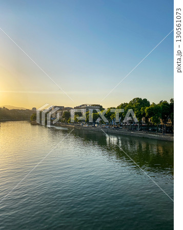 Calm cityscape on the river bank with trees, buildings and calm water under clear blue sky at sunset 130561073