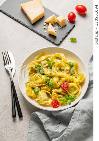 Tortellini pasta with parmesan, pesto and basil in a plate on a light background with tomato Tortellini pasta with parmesan, pesto and basil in a plate on a light background with tomato 130561094