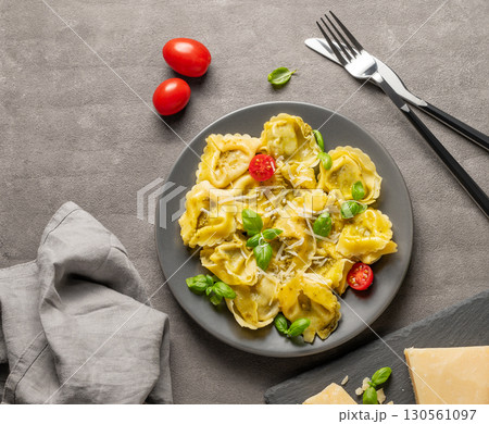 Tortellini pasta with parmesan, pesto and basil in a plate on a dark background with cheese, cutlery 130561097