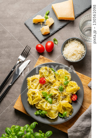 Tortellini pasta with parmesan, pesto and basil in a plate on a wooden board on a dark background Tortellini pasta with parmesan, pesto and basil in a plate on a wooden board on a dark background 130561098