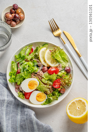 Tuna salad with cherry tomatoes, eggs, olives and cucumbers in a white plate on a light background Tuna salad with cherry tomatoes, eggs, olives and cucumbers in a white plate on a light background 130561101