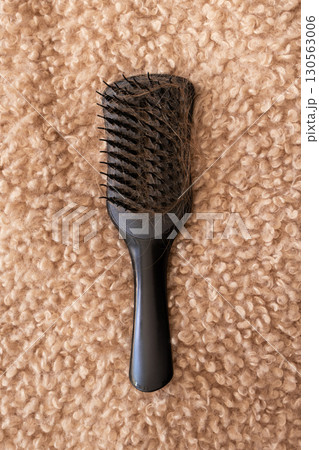 Black hairbrush with fallen hair on a fluffy beige background. Hair loss, shedding 130563006