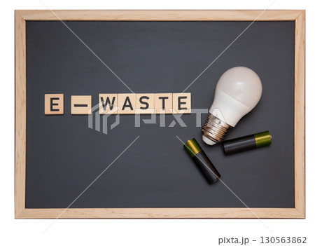 Chalkboard with the word "E-WASTE" made of wooden letters next to an LED light bulb and batteries 130563862