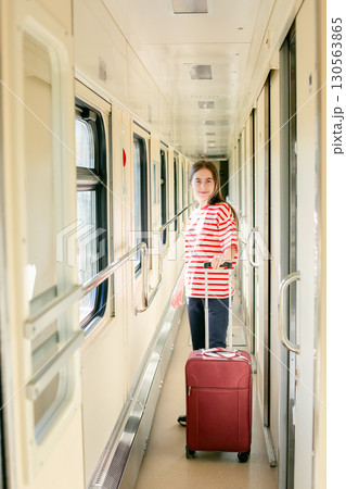 Girl red white striped shirt stands inside sunlit train corridor, expressing joy, confidence, travel 130563865